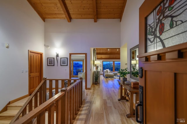 hall with beam ceiling, high vaulted ceiling, light wood-style flooring, an upstairs landing, and wood ceiling