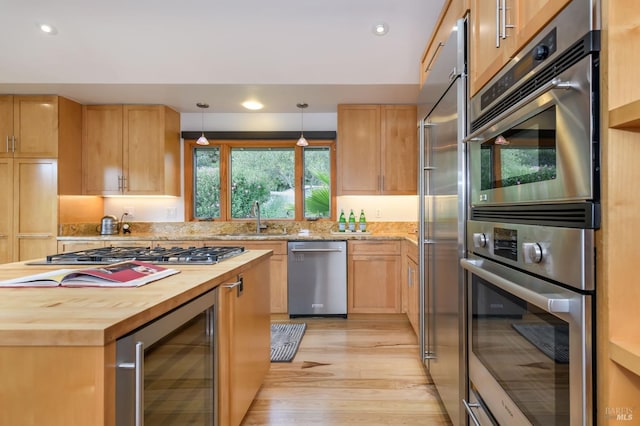 kitchen with appliances with stainless steel finishes, a sink, wooden counters, light wood-style flooring, and wine cooler