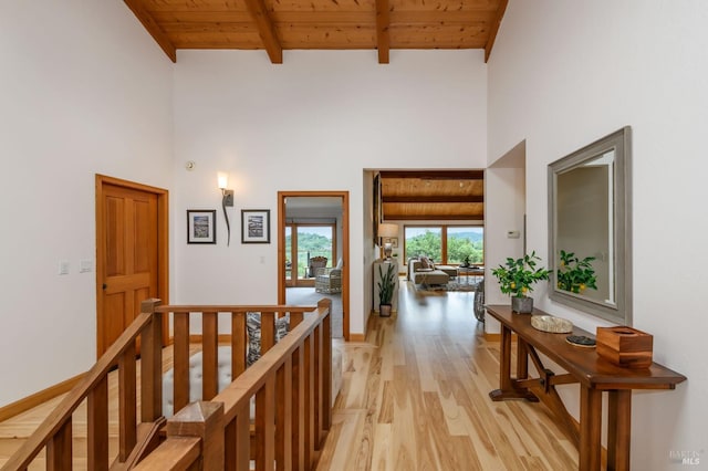 corridor featuring wooden ceiling, an upstairs landing, light wood-type flooring, and a towering ceiling
