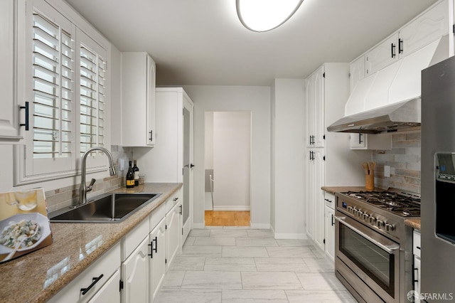 kitchen featuring appliances with stainless steel finishes, marble finish floor, backsplash, a sink, and baseboards