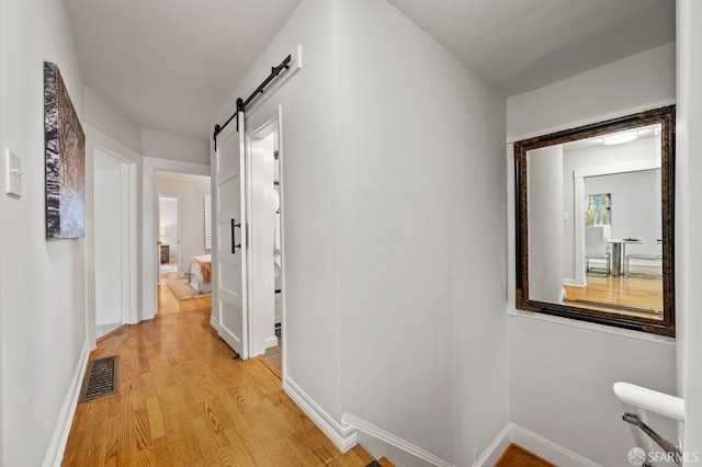 corridor featuring visible vents, baseboards, a barn door, and light wood-style floors