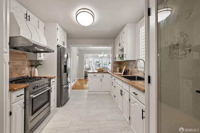 kitchen with under cabinet range hood, appliances with stainless steel finishes, white cabinetry, and a sink