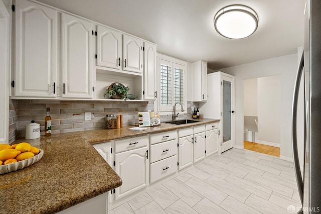 kitchen featuring freestanding refrigerator, decorative backsplash, white cabinets, a sink, and baseboards