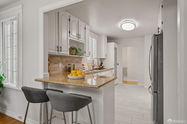 kitchen with white cabinetry, freestanding refrigerator, backsplash, baseboards, and a peninsula