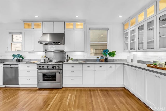 kitchen with appliances with stainless steel finishes, white cabinetry, wall chimney range hood, and light hardwood / wood-style flooring