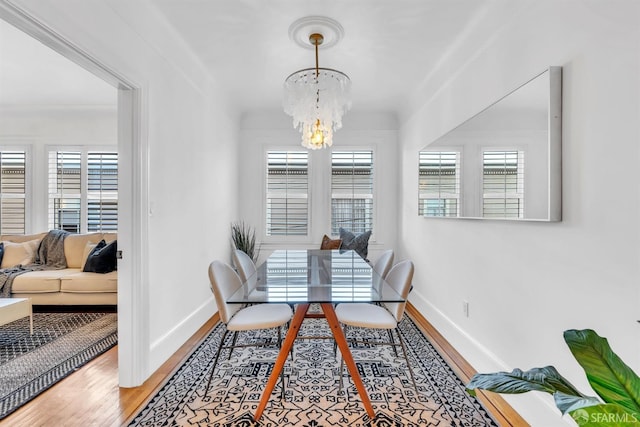 dining space with wood-type flooring, a notable chandelier, ornamental molding, and a healthy amount of sunlight