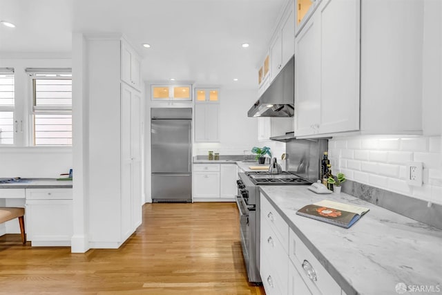 kitchen with premium appliances, light hardwood / wood-style flooring, light stone countertops, and white cabinetry