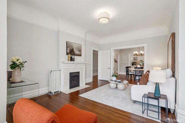 living area with an inviting chandelier, baseboards, a brick fireplace, and wood finished floors