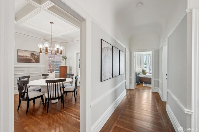 corridor with an inviting chandelier, ornamental molding, coffered ceiling, and dark wood-style floors