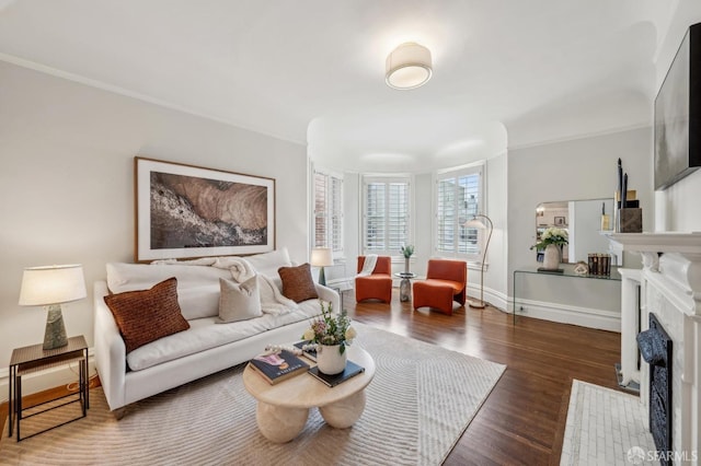 living area featuring baseboards, a fireplace with flush hearth, crown molding, and wood finished floors