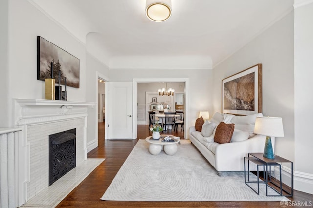 living area with an inviting chandelier, dark wood-style flooring, a brick fireplace, and baseboards