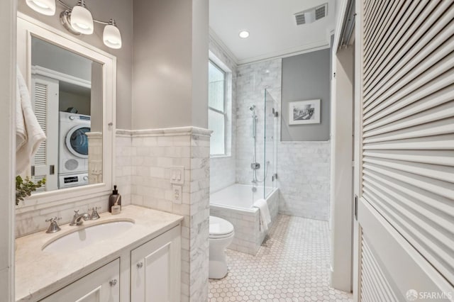 bathroom with tiled shower / bath combo, tile walls, stacked washer / drying machine, and tile patterned floors