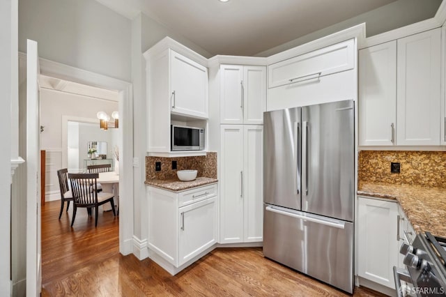 kitchen featuring white cabinetry, tasteful backsplash, light stone counters, light wood finished floors, and stainless steel appliances