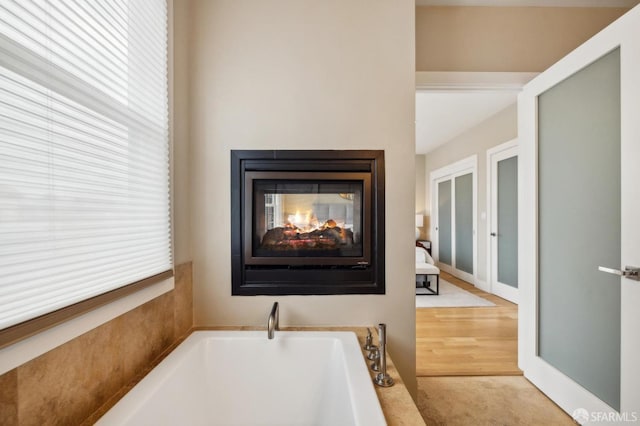 bathroom with a tub to relax in, a healthy amount of sunlight, and a multi sided fireplace