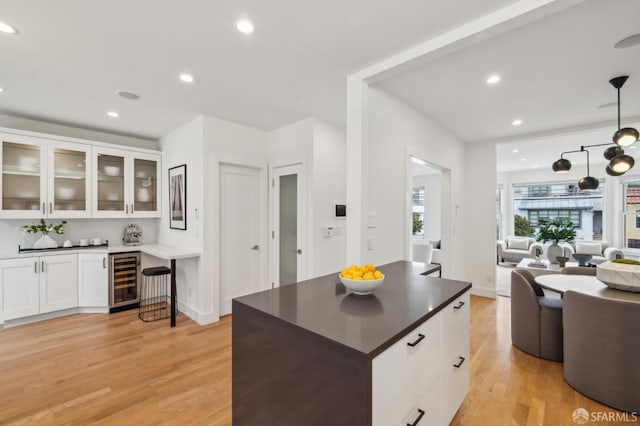 kitchen featuring wine cooler, hanging light fixtures, light wood-type flooring, a kitchen island, and white cabinets