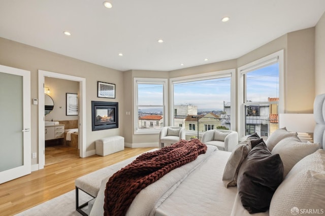 bedroom with ensuite bath, light hardwood / wood-style floors, and a multi sided fireplace