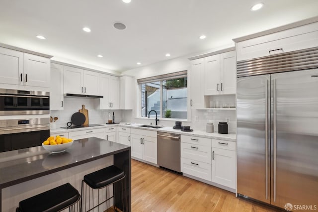 kitchen with sink, backsplash, white cabinets, light hardwood / wood-style floors, and stainless steel appliances