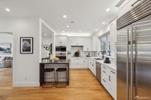 kitchen with appliances with stainless steel finishes, light hardwood / wood-style floors, sink, and white cabinets