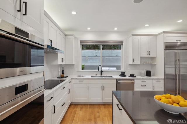 kitchen with stainless steel appliances, sink, white cabinets, and light hardwood / wood-style floors