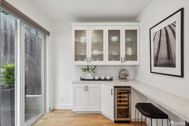 bar featuring wine cooler, white cabinetry, light wood-type flooring, light stone countertops, and decorative backsplash