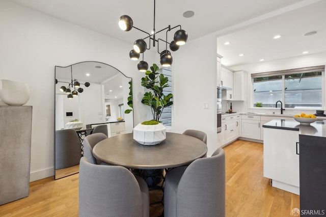 dining room with an inviting chandelier, sink, and light wood-type flooring