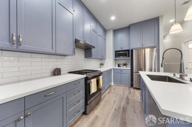 3004 26th St, San Francisco, CA 94110 - kitchen with stainless steel appliances, a sink, under cabinet range hood, light wood finished floors, and light countertops