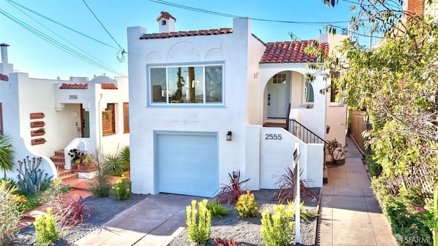 mediterranean / spanish-style home featuring a chimney, stucco siding, an attached garage, driveway, and a tiled roof