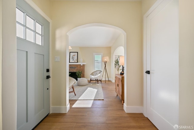 entryway featuring arched walkways, a brick fireplace, baseboards, and wood finished floors