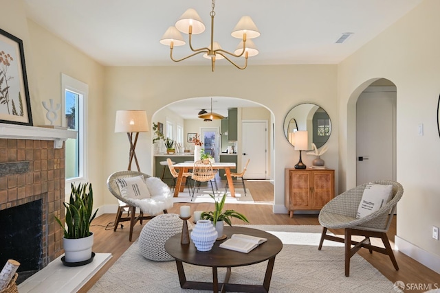 living area with a brick fireplace, a notable chandelier, baseboards, and wood finished floors