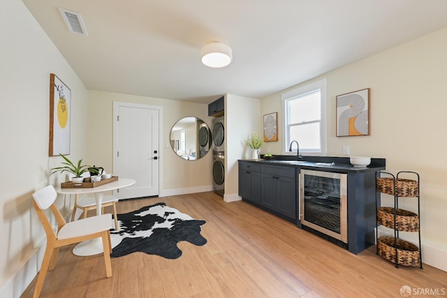 kitchen featuring wine cooler, light wood finished floors, stacked washer / drying machine, visible vents, and a sink