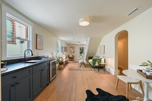 kitchen with arched walkways, wine cooler, visible vents, light wood-style flooring, and a sink