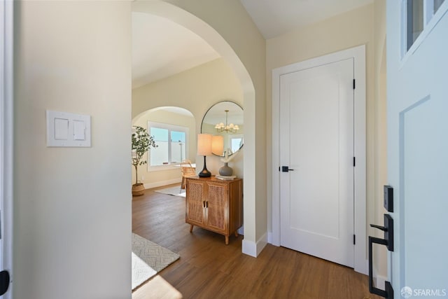 entryway with arched walkways, wood finished floors, and baseboards