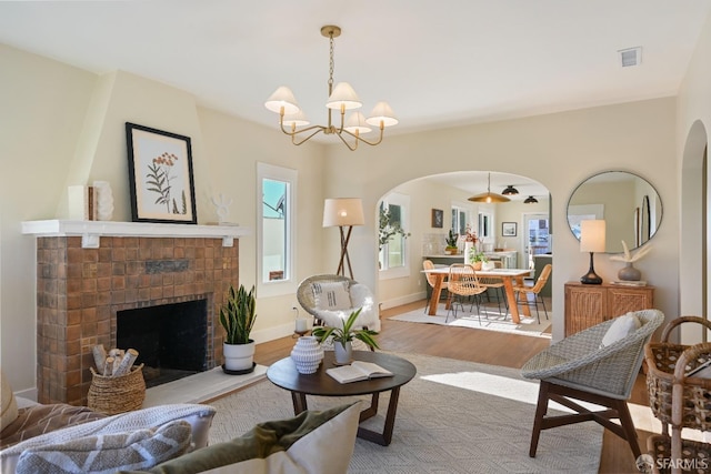 living area featuring baseboards, visible vents, arched walkways, wood finished floors, and a brick fireplace