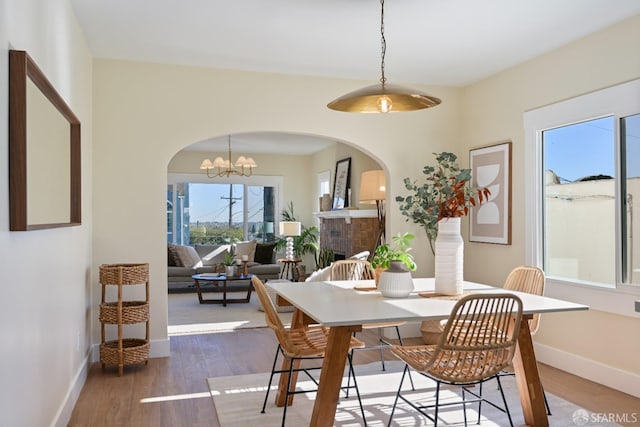 dining room with arched walkways, a fireplace, wood finished floors, baseboards, and an inviting chandelier