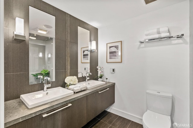 bathroom featuring toilet, double vanity, baseboards, and a sink