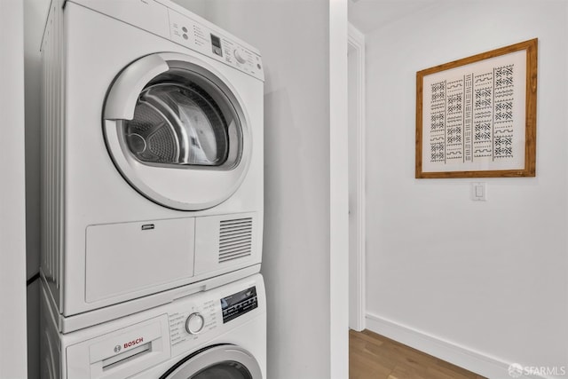 clothes washing area featuring laundry area, baseboards, stacked washer / dryer, and wood finished floors