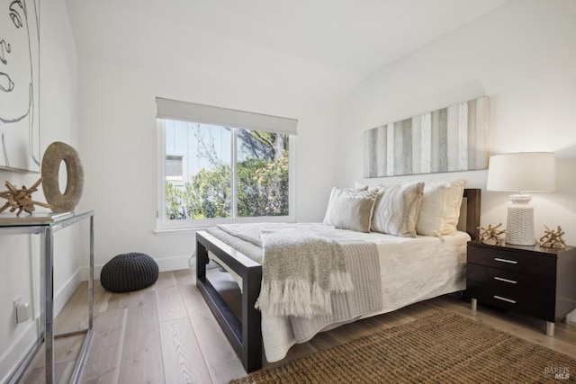 bedroom with baseboards, lofted ceiling, and wood finished floors