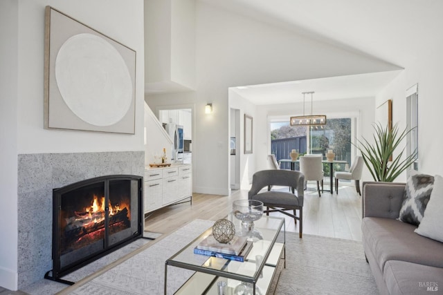 living area with light wood finished floors, a warm lit fireplace, high vaulted ceiling, and baseboards