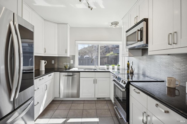 kitchen with a sink, tasteful backsplash, dark countertops, stainless steel appliances, and tile patterned flooring