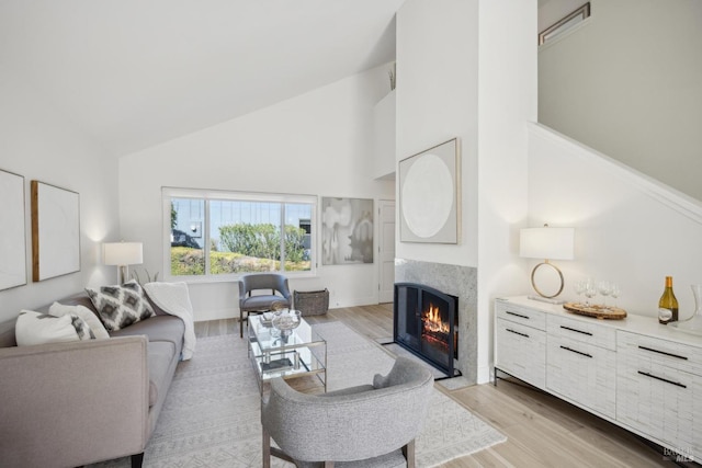 living room featuring a fireplace with flush hearth, light wood-style floors, and high vaulted ceiling