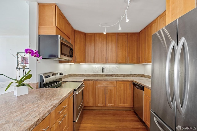 kitchen with light stone counters, appliances with stainless steel finishes, rail lighting, and light hardwood / wood-style flooring