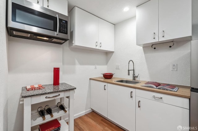 kitchen featuring light hardwood / wood-style floors, white cabinetry, butcher block counters, and sink