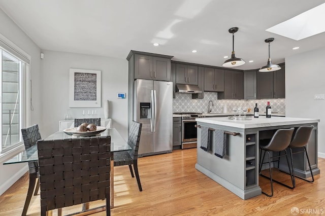 kitchen featuring a skylight, a kitchen island with sink, hanging light fixtures, and appliances with stainless steel finishes