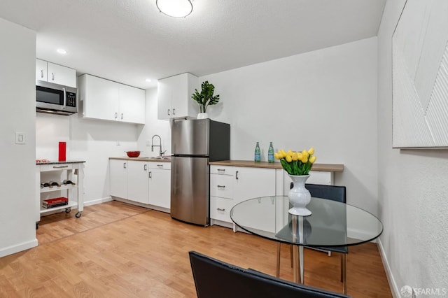 kitchen with stainless steel appliances, white cabinetry, light hardwood / wood-style floors, and sink