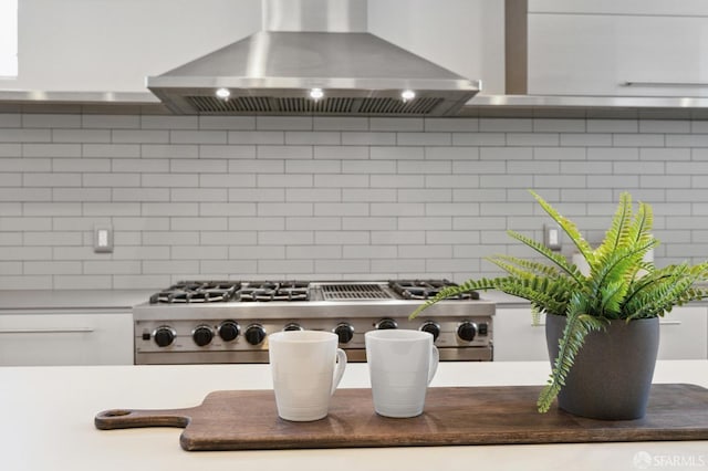 room details with stainless steel gas cooktop, wall chimney exhaust hood, tasteful backsplash, and white cabinetry