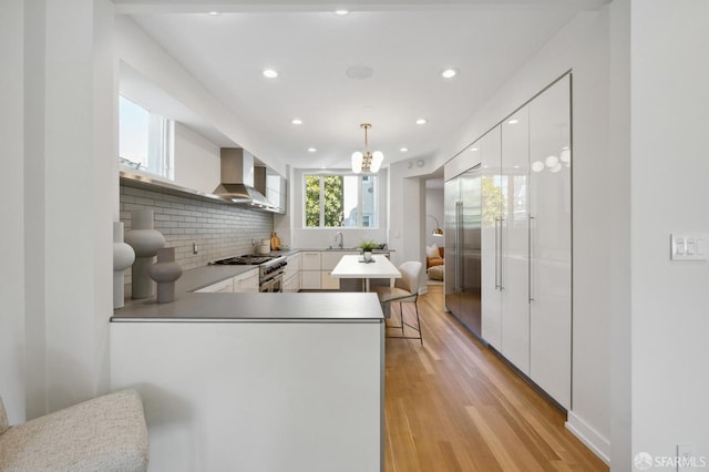 kitchen with white cabinets, decorative light fixtures, kitchen peninsula, and wall chimney range hood