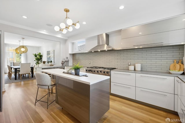 kitchen featuring decorative light fixtures, light wood-type flooring, wall chimney range hood, and white cabinetry