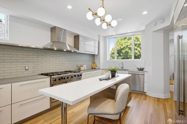 kitchen featuring white cabinets, wall chimney exhaust hood, premium appliances, light hardwood / wood-style flooring, and decorative light fixtures