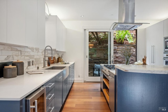 kitchen featuring island range hood, modern cabinets, a sink, beverage cooler, and light wood-style flooring