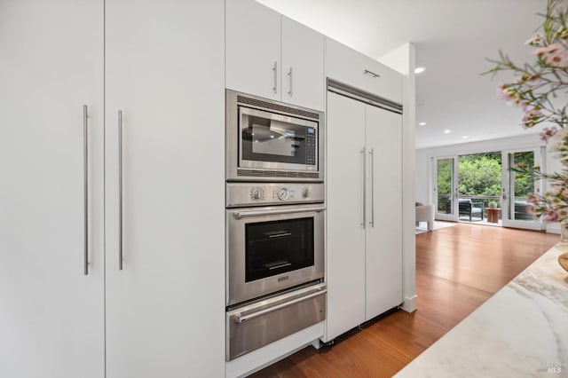 kitchen featuring built in appliances, wood finished floors, light stone countertops, white cabinets, and a warming drawer